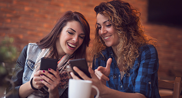 Two women at coffee shop on their smart phones laughing